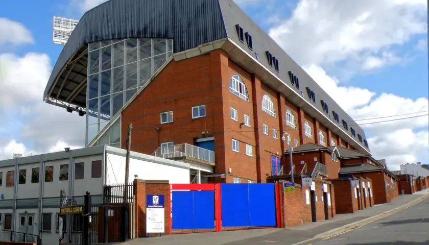 Widok na ceglany budynek stadionu Crystal Palace z charakterystycznym zadaszeniem i przeszkloną ścianą.