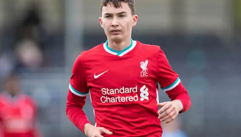 Młody piłkarz Mateusz Musiałowski w czerwonej koszulce Liverpoolu, z dumą nosi herb klubu.