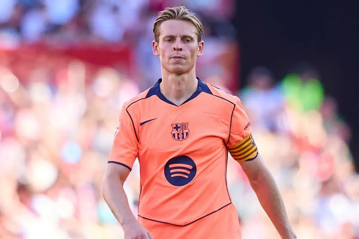 Frenkie de Jong w pomarańczowej koszulce FC Barcelony z opaską kapitana na ramieniu, skupiony na boisku.