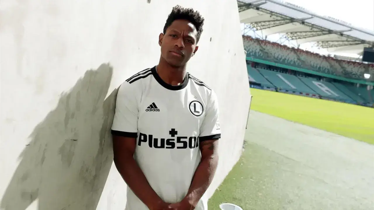 Joel Valencia w białej koszulce Legii Warszawa, z logo Plus500, na tle stadionu.