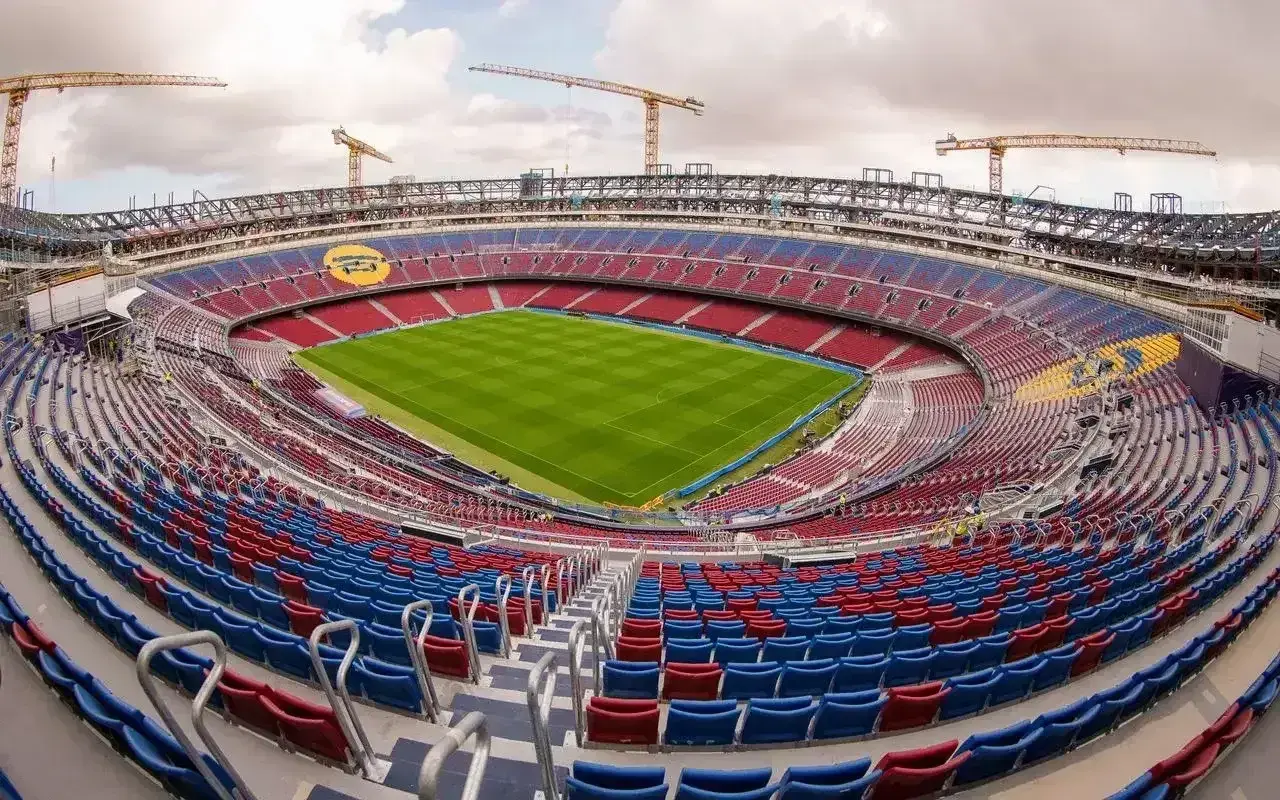 Widok na Camp Nou, największy stadion w Hiszpanii, w trakcie modernizacji. Żurawie budowlane górują nad trybunami w barwach czerwono-niebieskich.