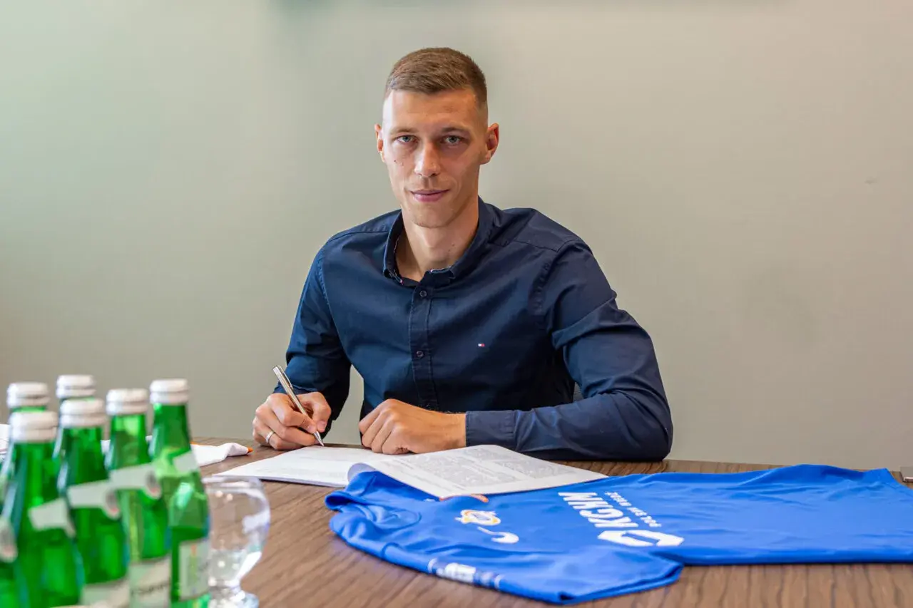 Dominik Hładun podpisuje kontrakt, obok leży niebieska koszulka.