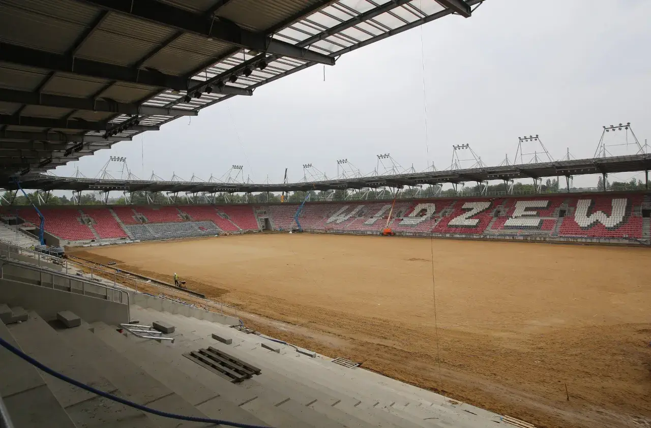 Trwa rozbudowa stadionu Widzewa. Na piaszczystym boisku widać prace budowlane i krzesełka w barwach klubu.