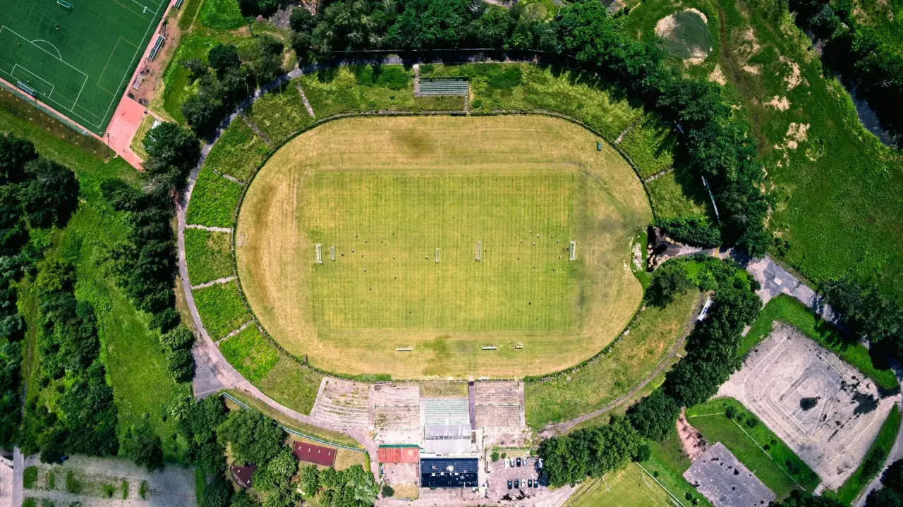 Widok z lotu ptaka na stadion Szombierki Bytom z zieloną murawą, trybunami i otaczającą go zielenią.