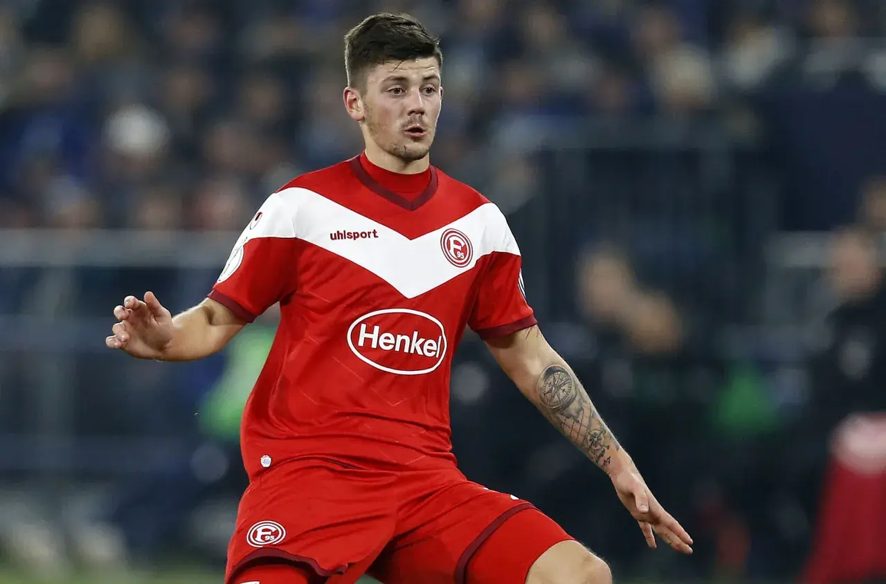 Jeden z zawodników Hertha BSC w czerwonej koszulce z białymi elementami i logo "Henkel" na piersi, z tatuażem kompasu na ramieniu.