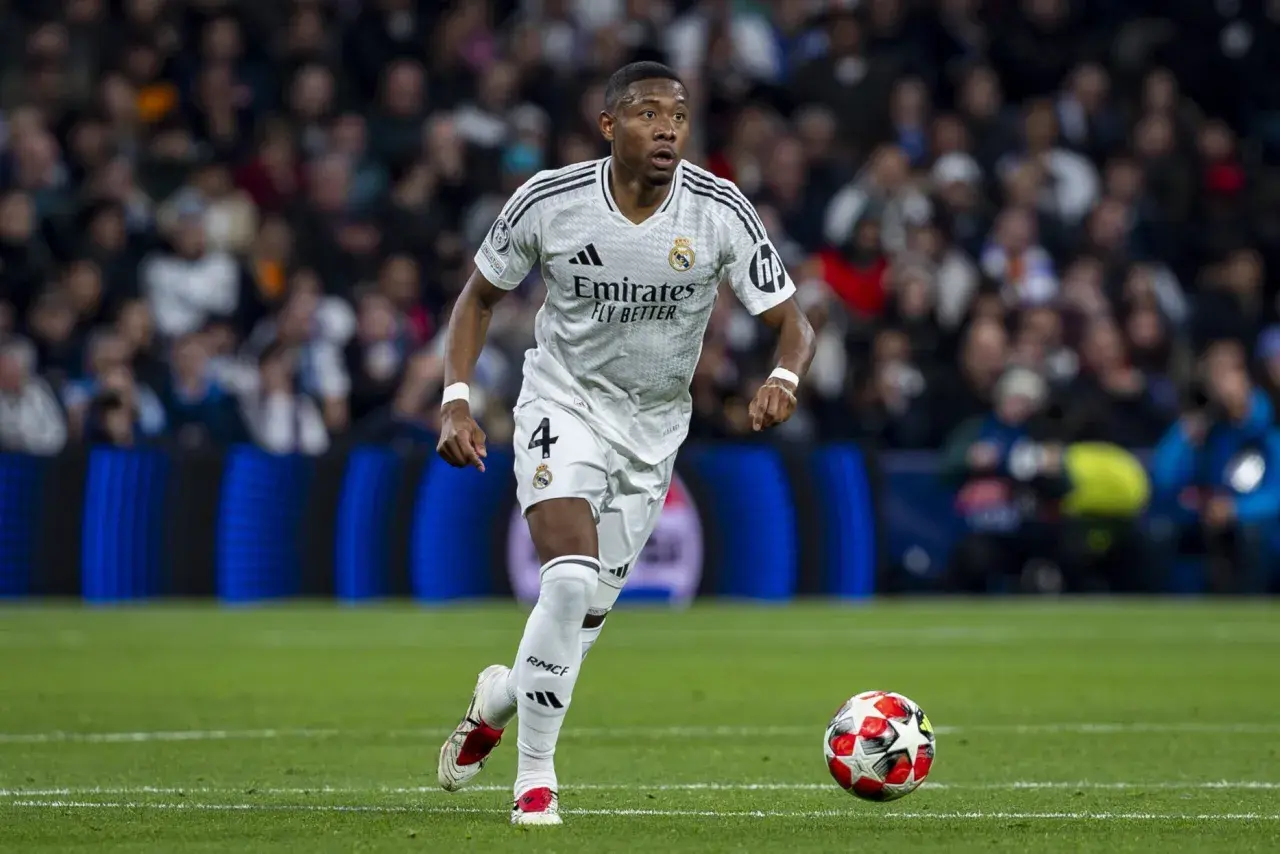 David Alaba w białej koszulce Realu Madryt z numerem 4 biegnie z piłką na murawie, skupiony na grze.