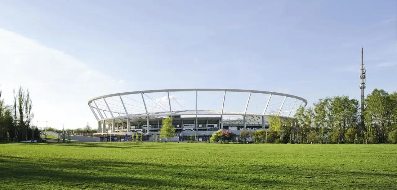 Nowoczesny Stadion Śląski otoczony zielenią, z charakterystyczną, okrągłą konstrukcją dachu.