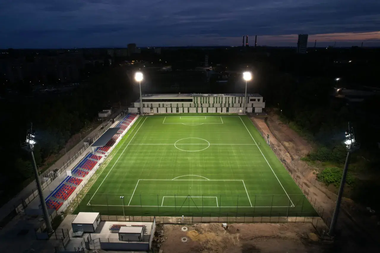 Piękny, oświetlony stadion Polonii Bytom nocą. Zielona murawa i czerwono-niebieskie trybuny czekają na kibiców.