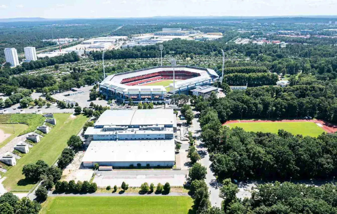 Widok z lotu ptaka na Max-Morlock-Stadion otoczony zielenią, z pobliskimi budynkami i boiskiem sportowym.