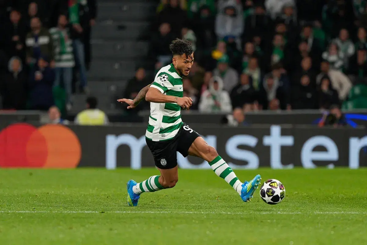 Piłkarz Sporting CP w zielono-białej koszulce drybluje z piłką na boisku.