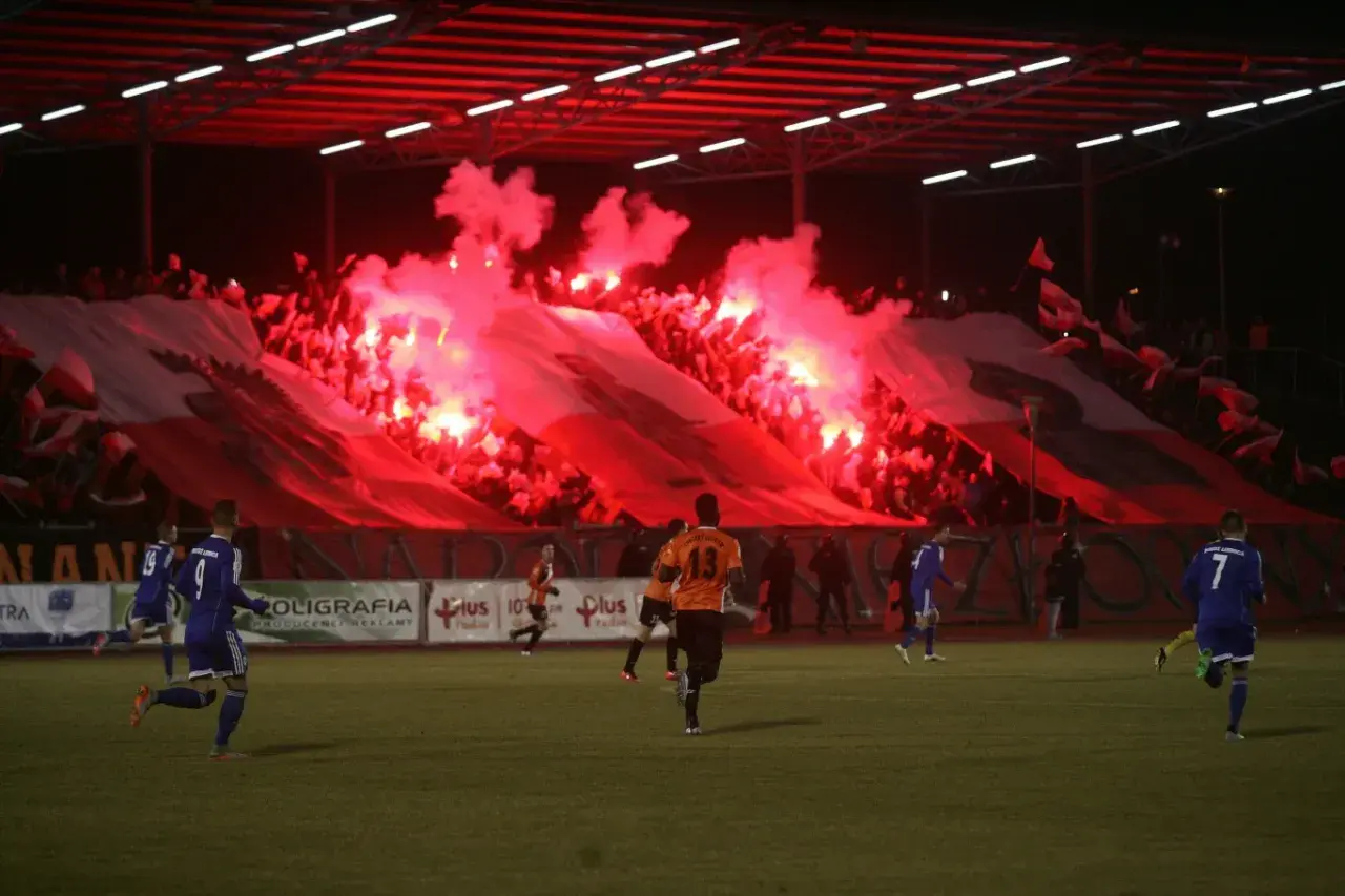 Chrobry Głogów stadion w ogniu rac! Kibice tworzą biało-czerwoną oprawę, a piłkarze grają na murawie.