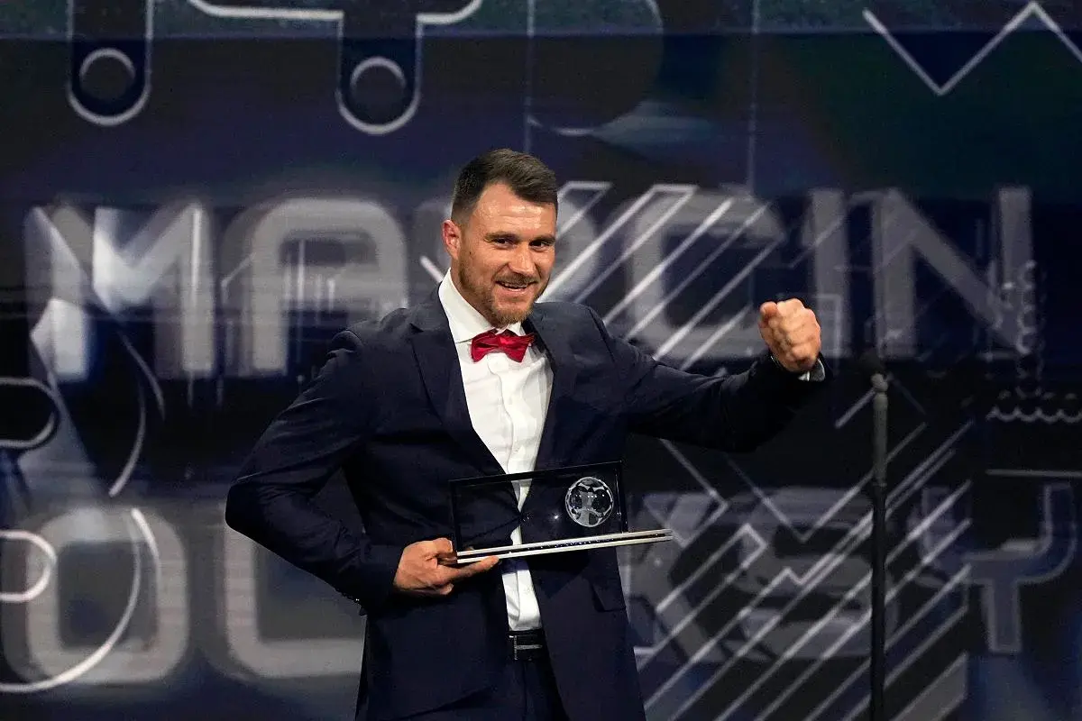 Piłkarz w garniturze z czerwoną muszką odbiera nagrodę Ferenca Puskasa, ciesząc się z sukcesu.