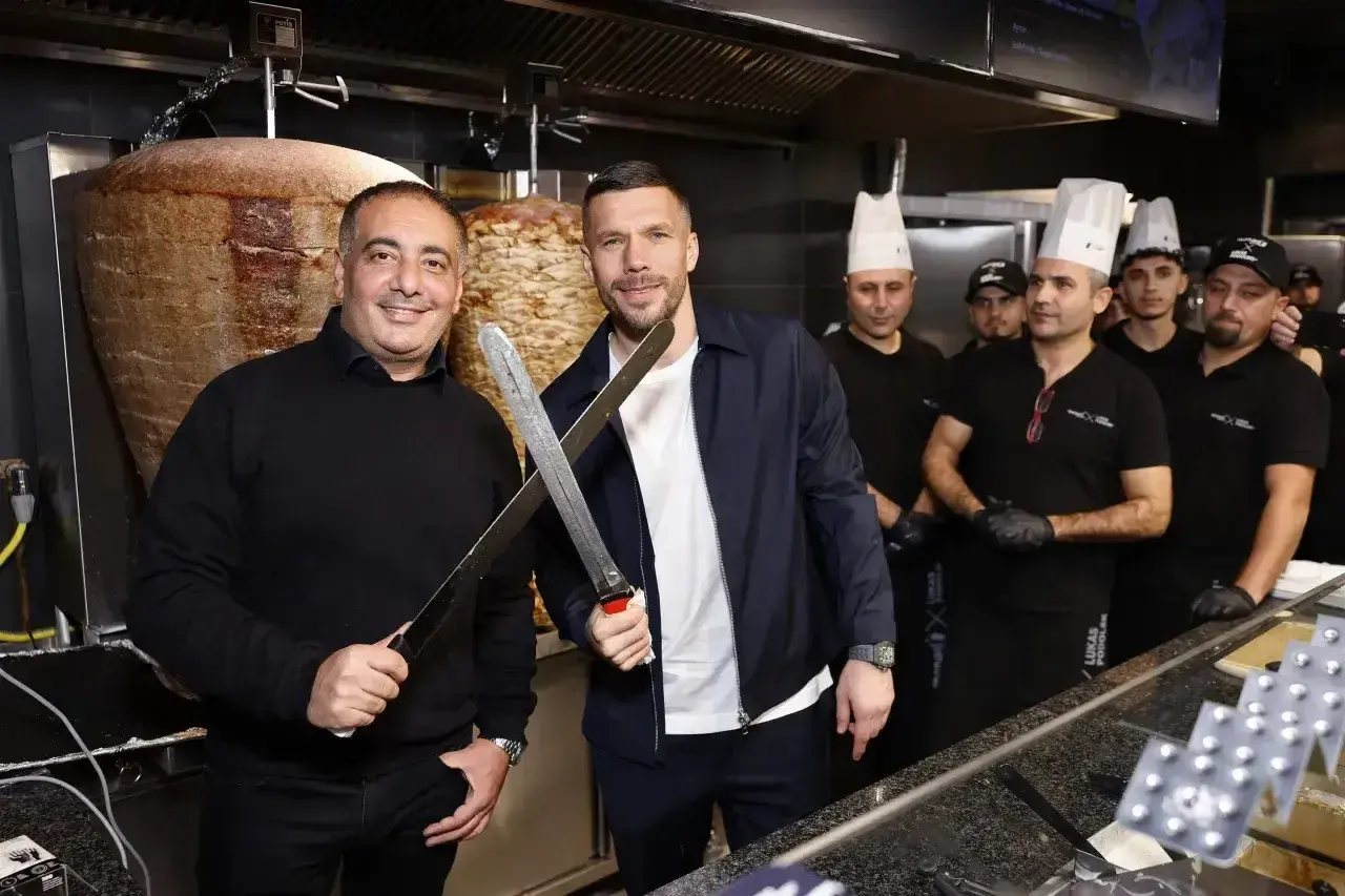 Lukas Podolski z nożami w ręku, obok niego pracownicy jego restauracji z kebabem.