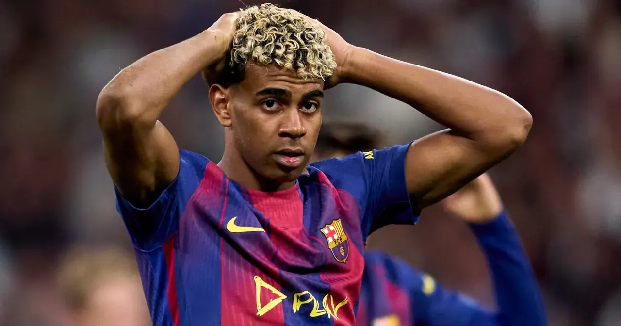 Młody piłkarz Lamine Yamal w koszulce FC Barcelona z blond lokami, trzymający się za głowę.