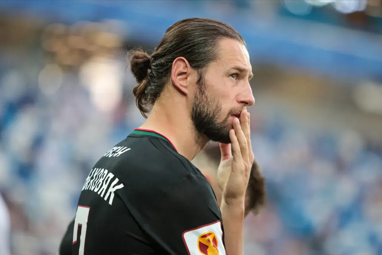 Grzegorz Krychowiak w czarnej koszulce, z włosami związanymi w kok, zamyślony na boisku.