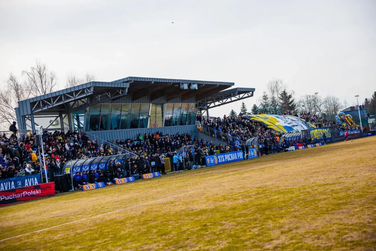 Widok na trybuny stadionu Avia Świdnik, wypełnione kibicami. W tle widać zadaszenie i drzewa.