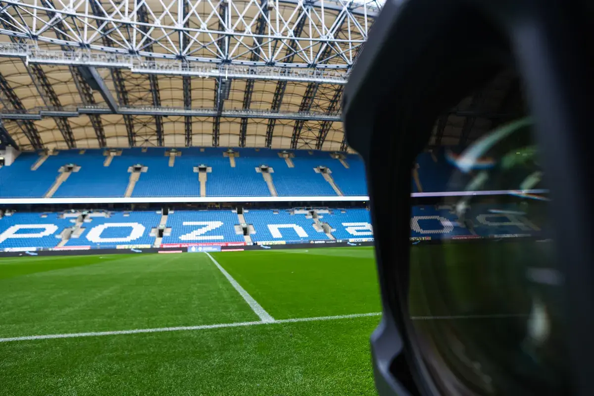 Pusta trybuna stadionu Lecha Poznań. Widoczne niebieskie sektory i miejsca, zielona murawa.