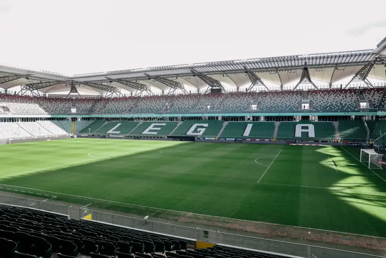 Puste trybuny stadionu Wojska Polskiego czekają na kibiców. Na zielonej murawie widać białe linie boiska.