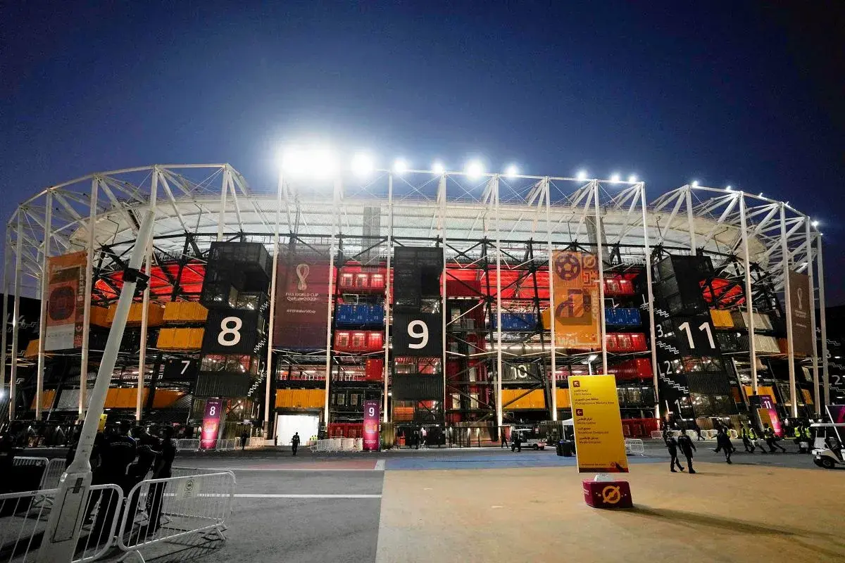 Nocny widok na **stadion z kontenerów Katar** z numerowanymi sekcjami i banerami Mistrzostw Świata FIFA 2022.