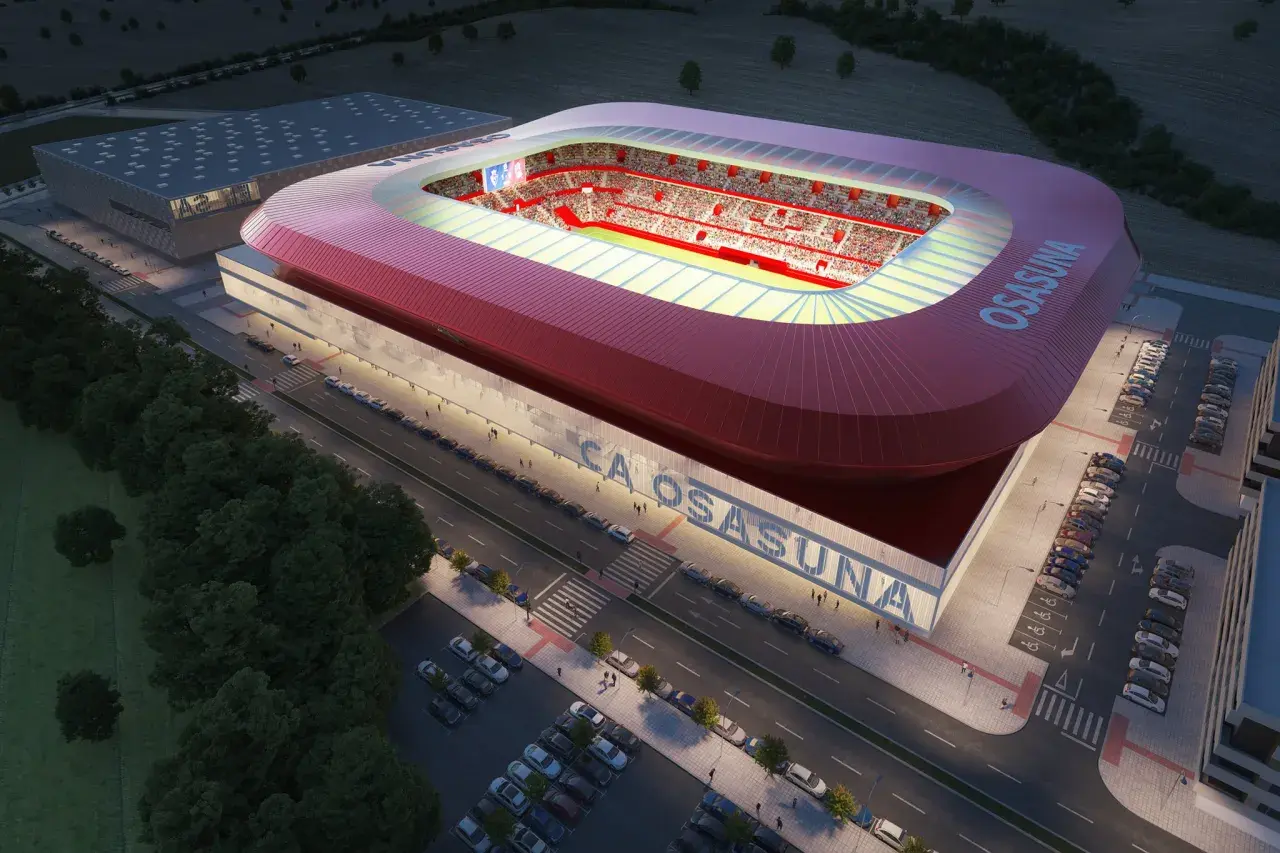 Nowoczesny stadion **El Sadar** w nocy, z czerwonym dachem i trybunami wypełnionymi kibicami. Obok budynek treningowy i parkingi.