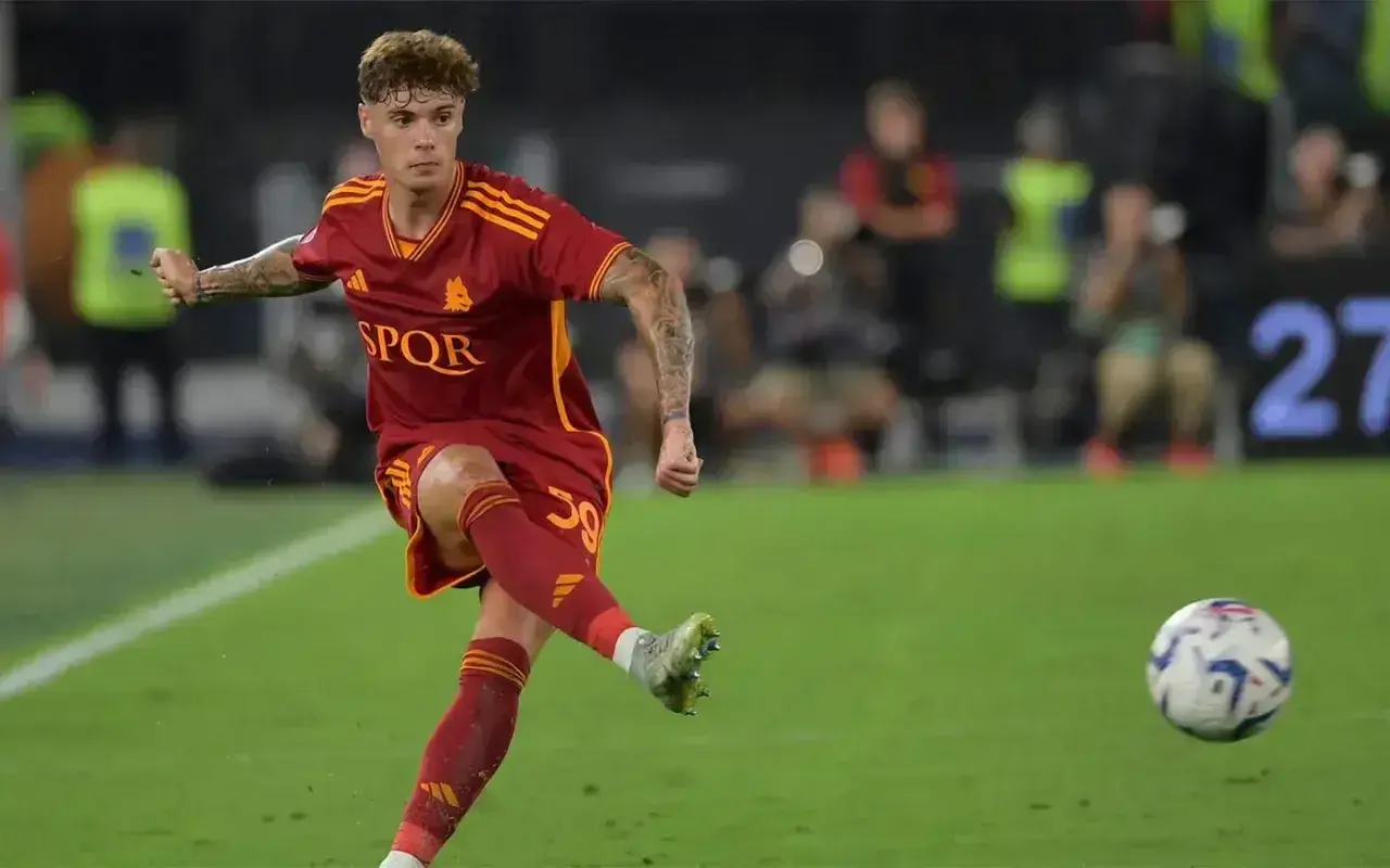 Nicola Zalewski w akcji, kopie piłkę na boisku w czerwonej koszulce AS Roma.