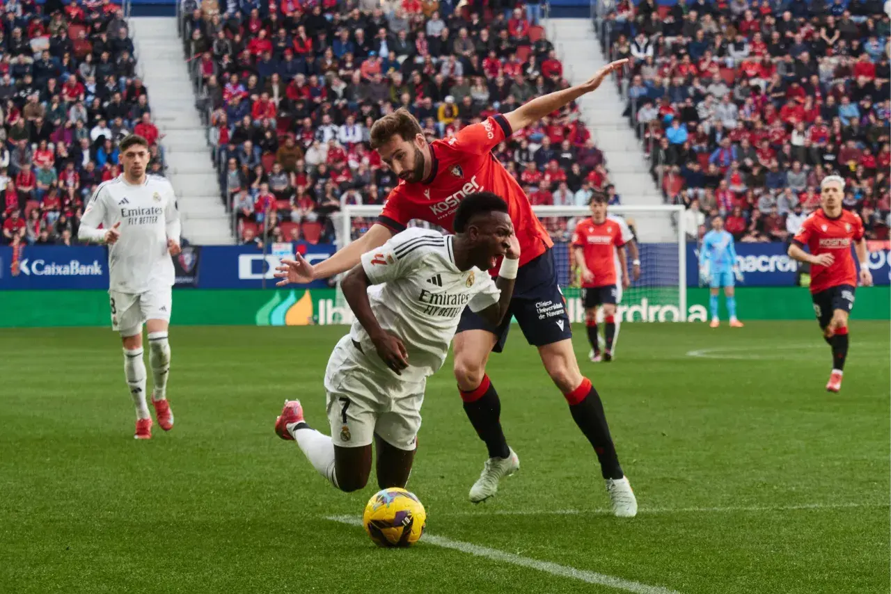 Piłkarze Real Madryt i Osasuna walczą o piłkę na murawie. W tle trybuny pełne kibiców.
