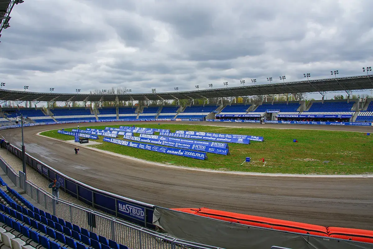 Pusty stadion żużlowy Orzeł Łódź z niebieskimi trybunami i torem żużlowym.
