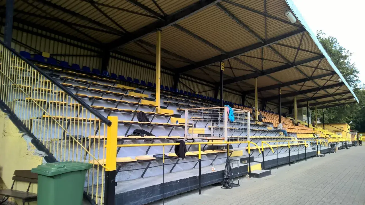 Puste trybuny stadionu Gryf Wejherowo, z żółtymi i niebieskimi siedzeniami pod zadaszeniem.