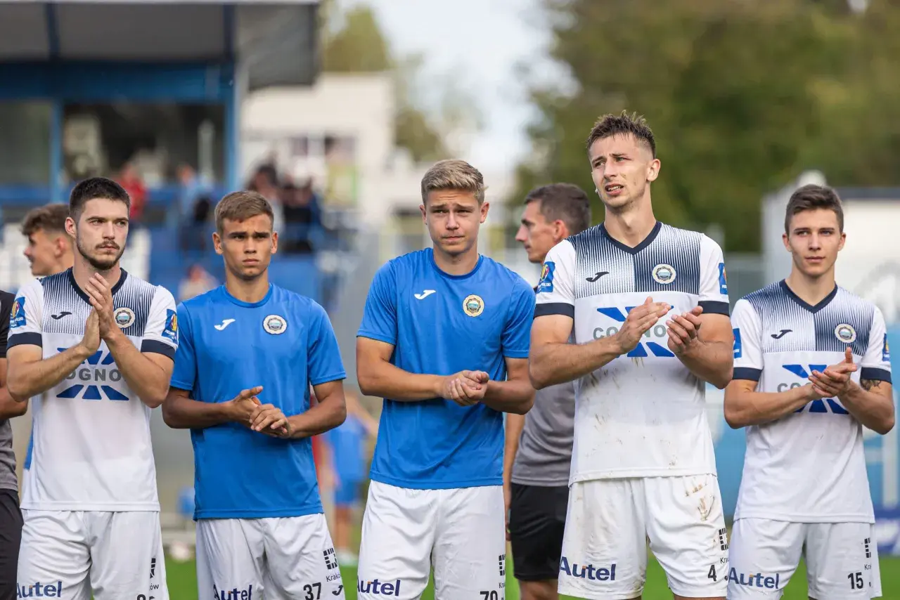 Pięciu młodych piłkarzy Hutnika Kraków w strojach klubowych stoi w rzędzie, klaszcząc.