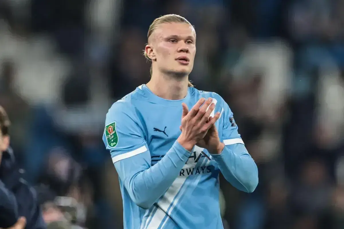 Erling Haaland w błękitnej koszulce Manchesteru City, z pucharem Carabao Cup na rękawie, klaszcze na boisku.