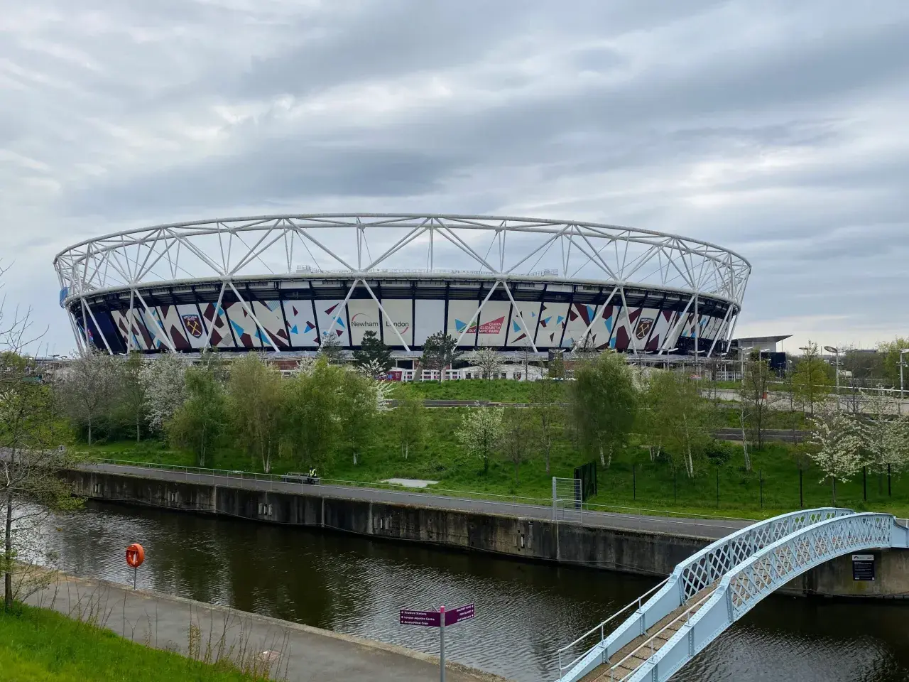 Ogromny stadion West Ham United z charakterystycznym logo klubu, otoczony zielenią i kanałem wodnym.