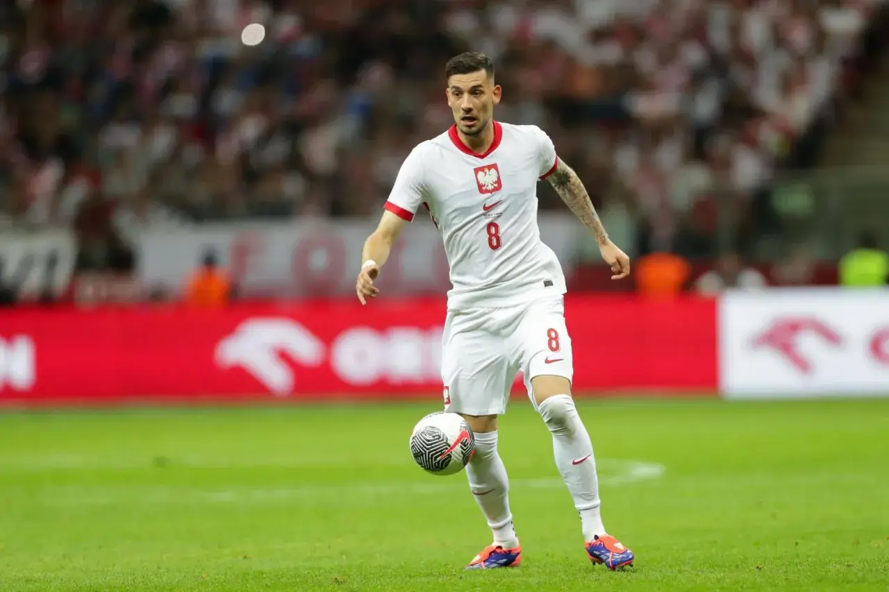 Jakub Moder w białej koszulce z numerem 8, z piłką przy nodze na boisku.