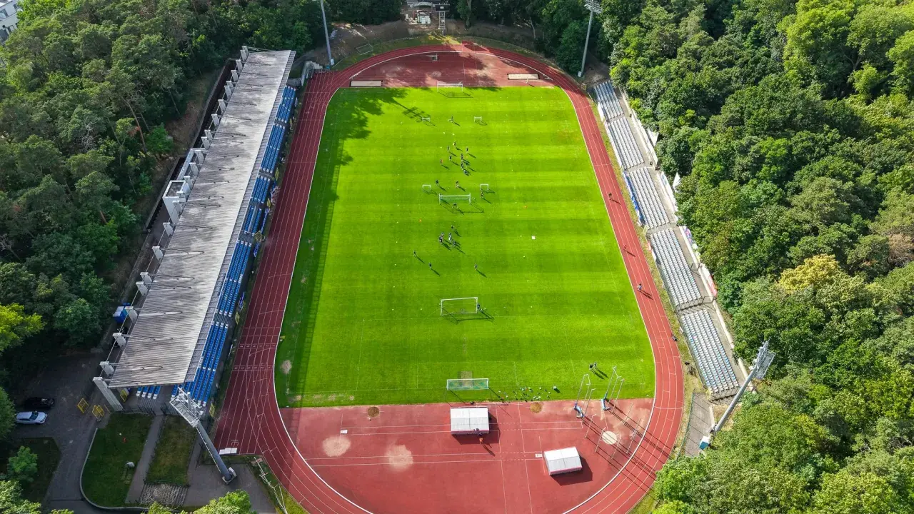 Piłkarze trenują na zielonej murawie stadionu Floty Świnoujście, otoczonego drzewami.
