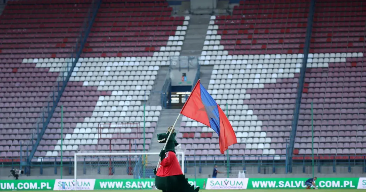 Maskotka Wisły Kraków z flagą na tle stadionu.
