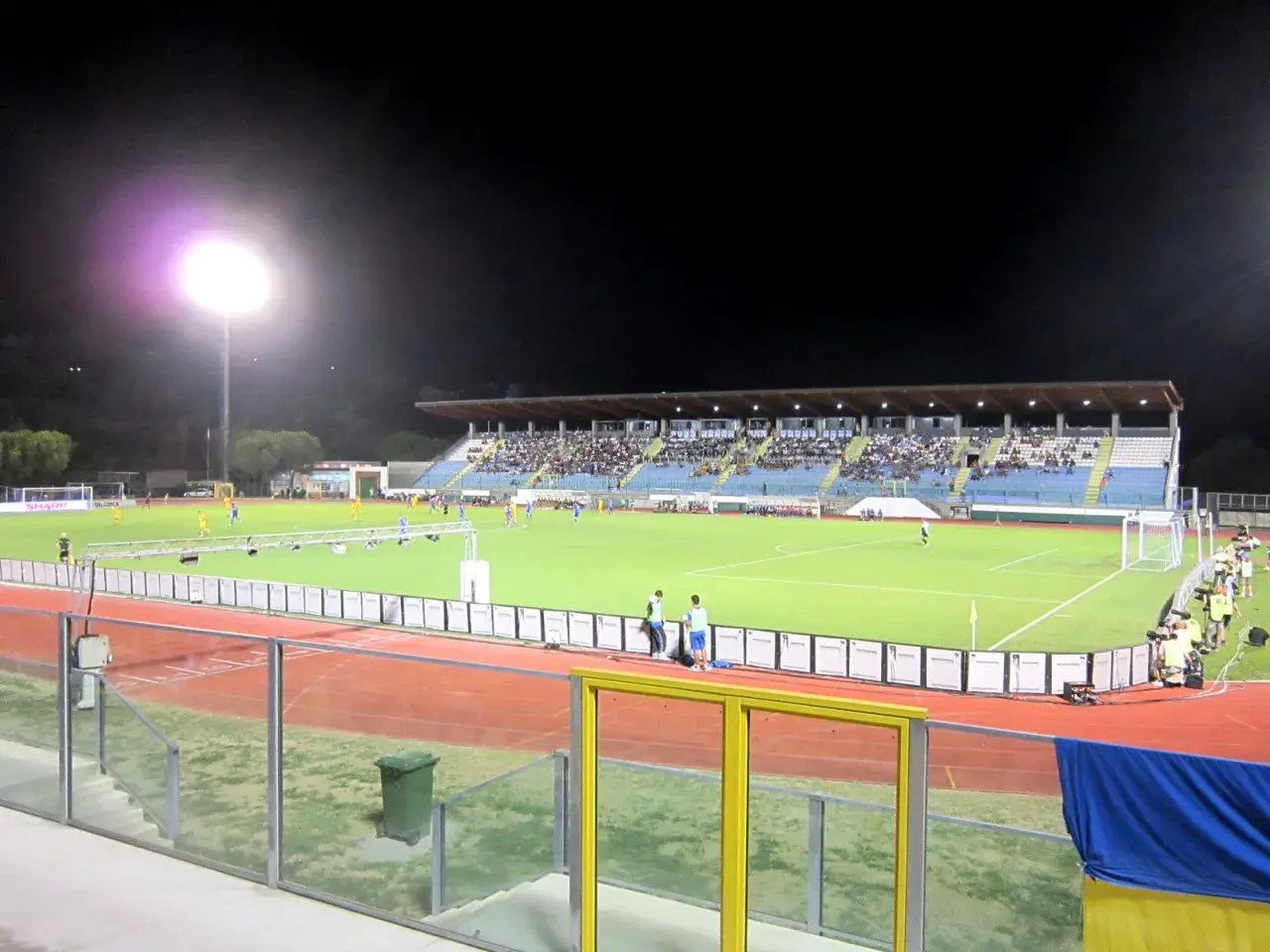 Wieczorny mecz na stadionie w San Marino. Piłkarze biegają po zielonej murawie, a trybuny wypełnia publiczność.
