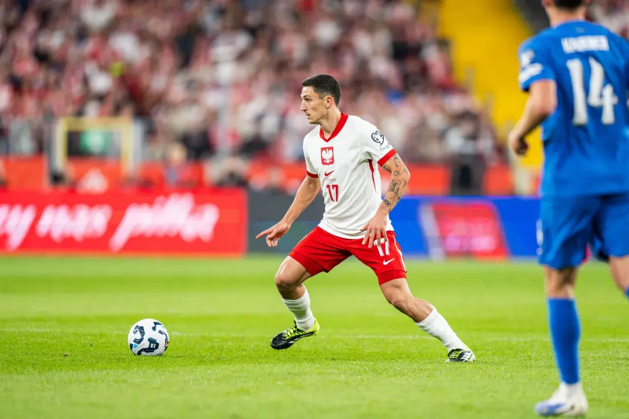 Bartosz Slisz w białej koszulce z orłem na piersi, w akcji na boisku.
