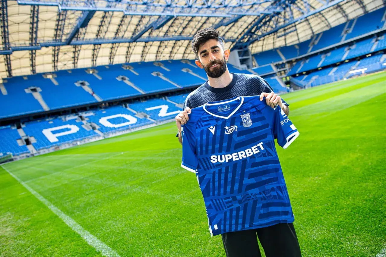 Ali Gholizadeh prezentuje nową koszulkę Lecha Poznań na tle stadionu.