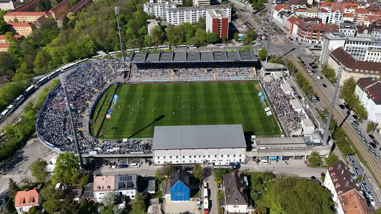 Widok z lotu ptaka na tętniący życiem tsv monachium stadion, pełen kibiców. Piłkarze rozgrywają mecz na zielonej murawie.
