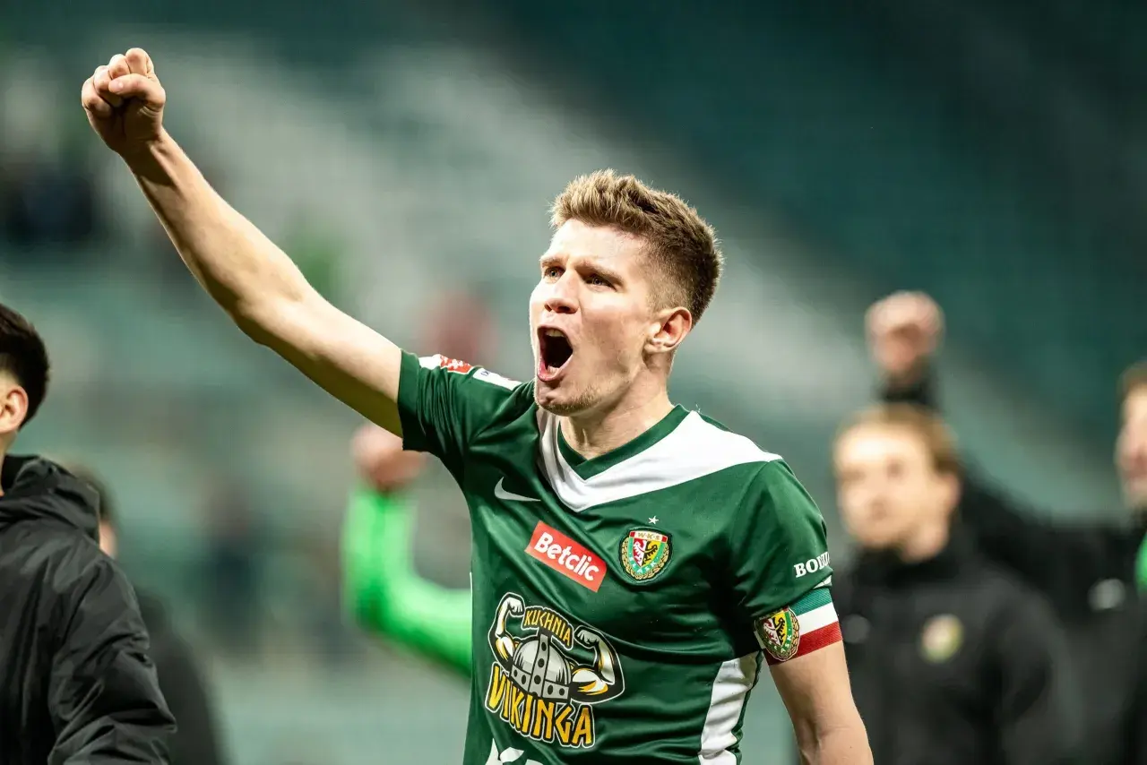 Piłkarz w zielonej koszulce z podniesioną pięścią świętuje awans do ekstraklasy.