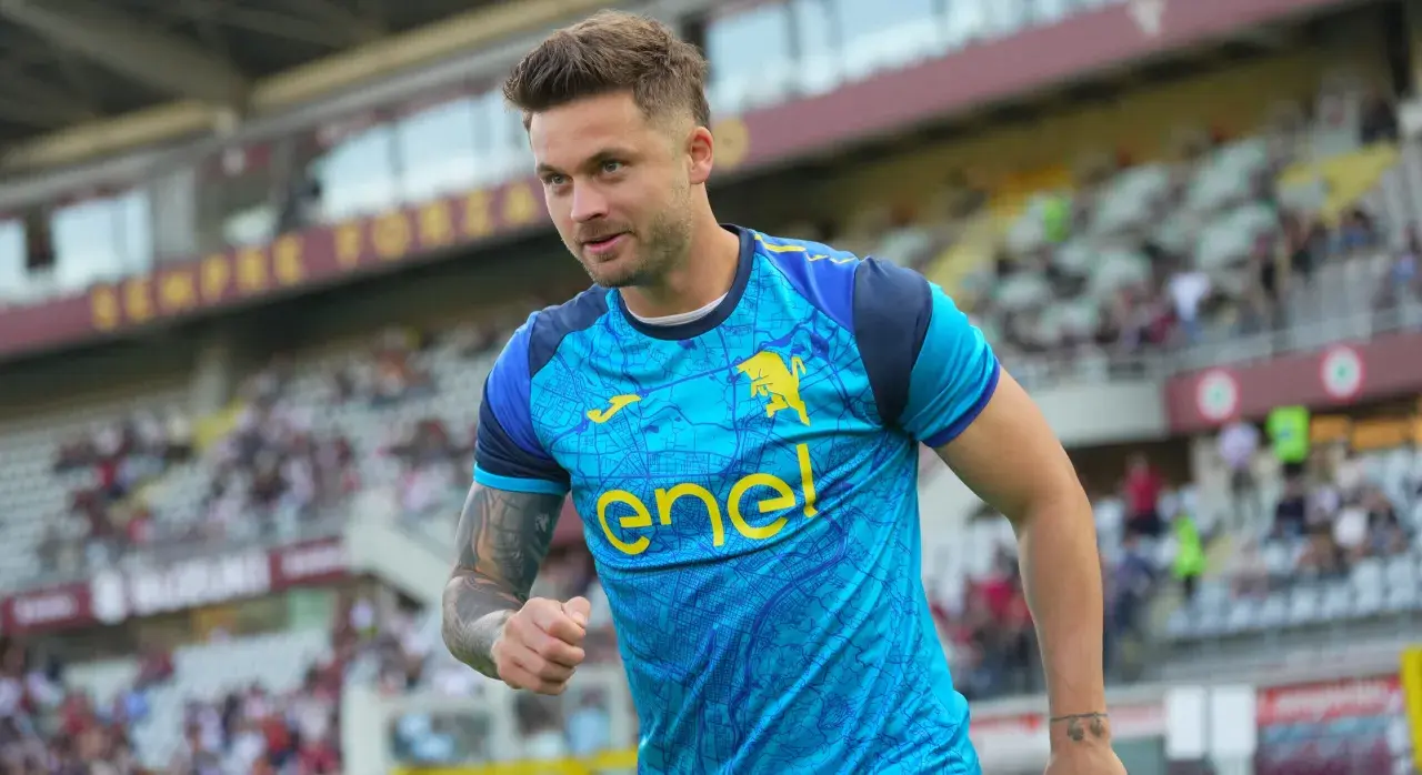 Piłkarz w błękitnej koszulce z żółtym logo "enel" i bykiem, widać trybuny stadionu. To moment, kiedy gra Linetty.
