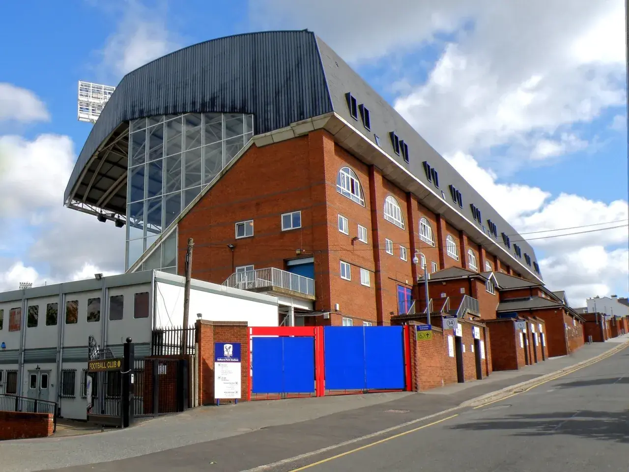 Widok na ceglany budynek stadionu Crystal Palace z charakterystycznym zadaszeniem i przeszkloną ścianą.