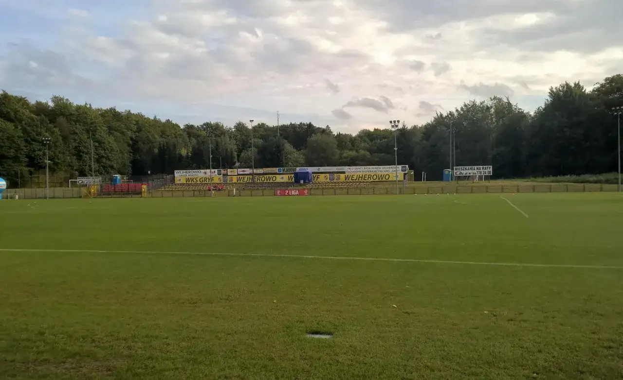 Stadion WKS Gryf Wejherowo z trybunami, banerami i zieloną murawą.