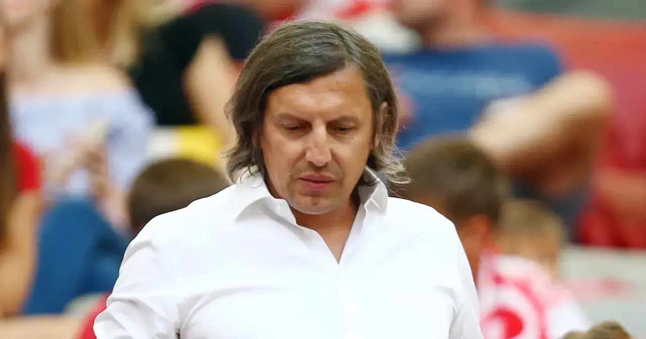 Jacek Bąk, były piłkarz, w białej koszuli, zamyślony, na tle trybun.