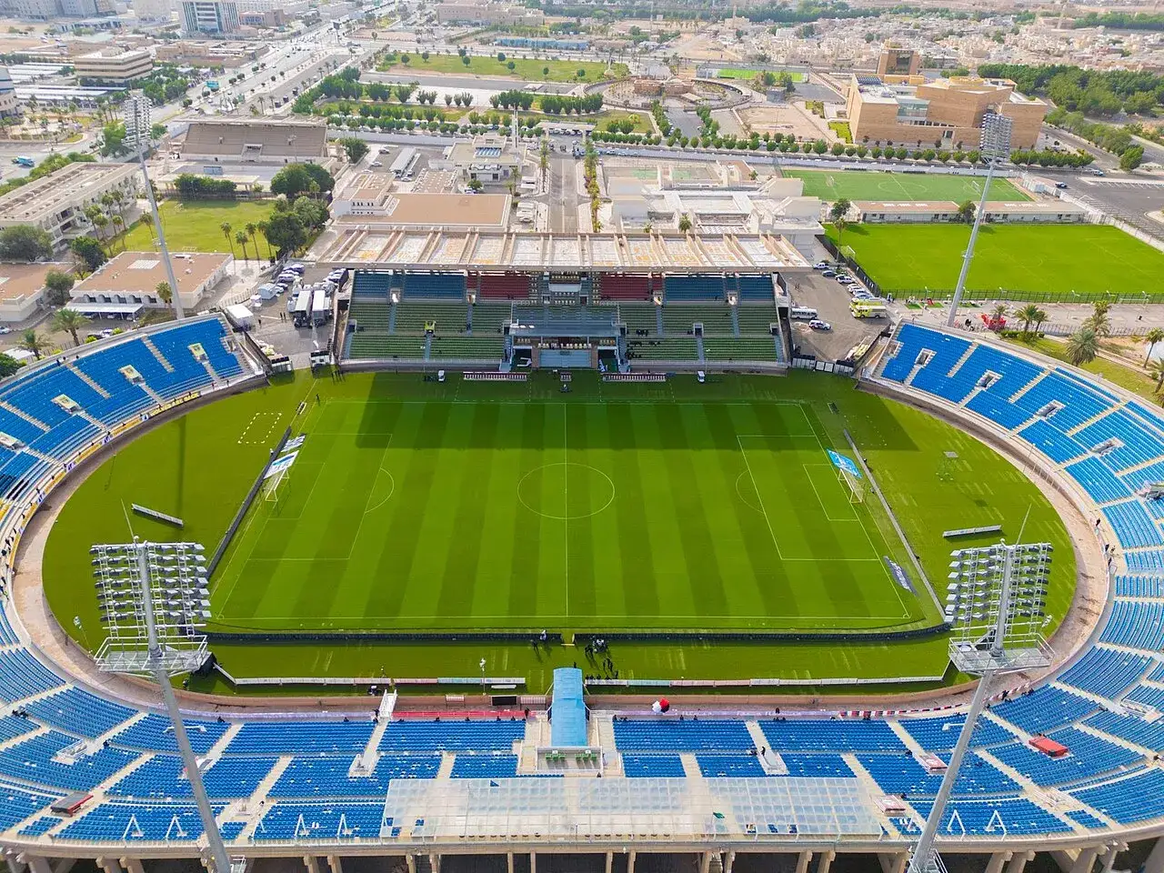 Widok z lotu ptaka na stadion King Abdullah Sports City z zieloną murawą i niebieskimi trybunami.