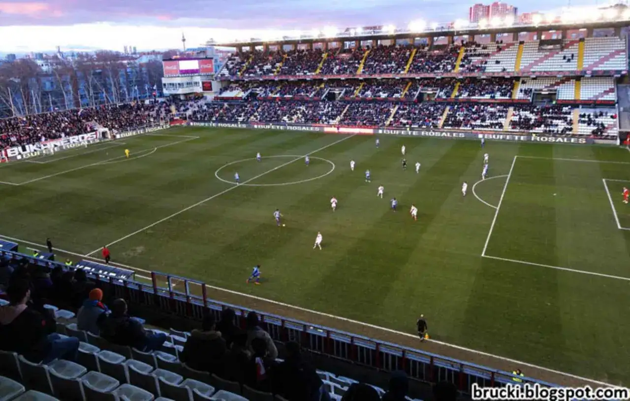Mecz na stadionie Rayo Vallecano. Piłkarze biegają po zielonej murawie, a trybuny wypełniają kibice.