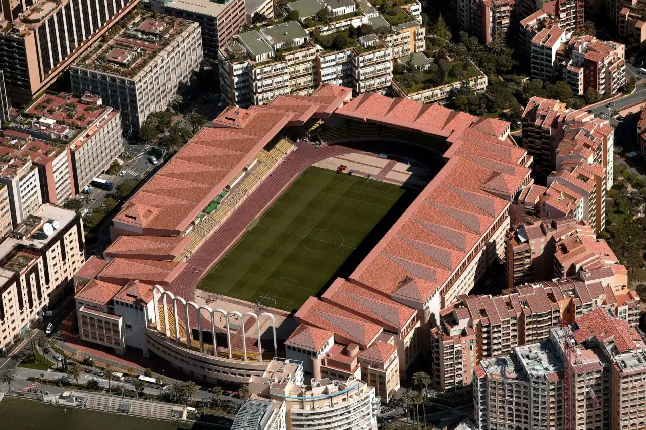 Stadion Louis II w Monako, znany jako as monaco stadion, z zieloną murawą i bieżnią, otoczony budynkami mieszkalnymi.