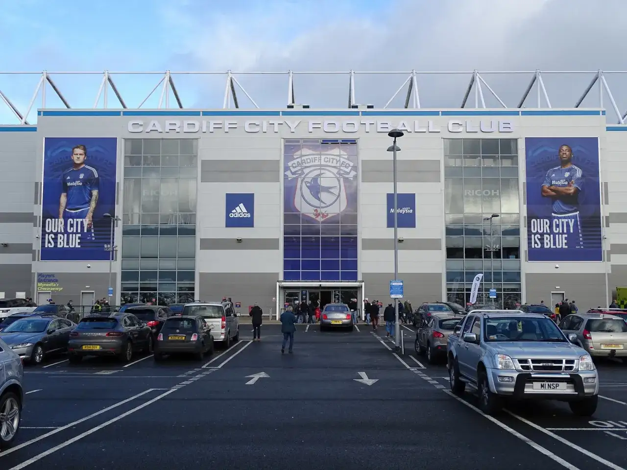 Widok na Cardiff City Stadium z parkingiem. Na fasadzie widnieje logo klubu i hasło 