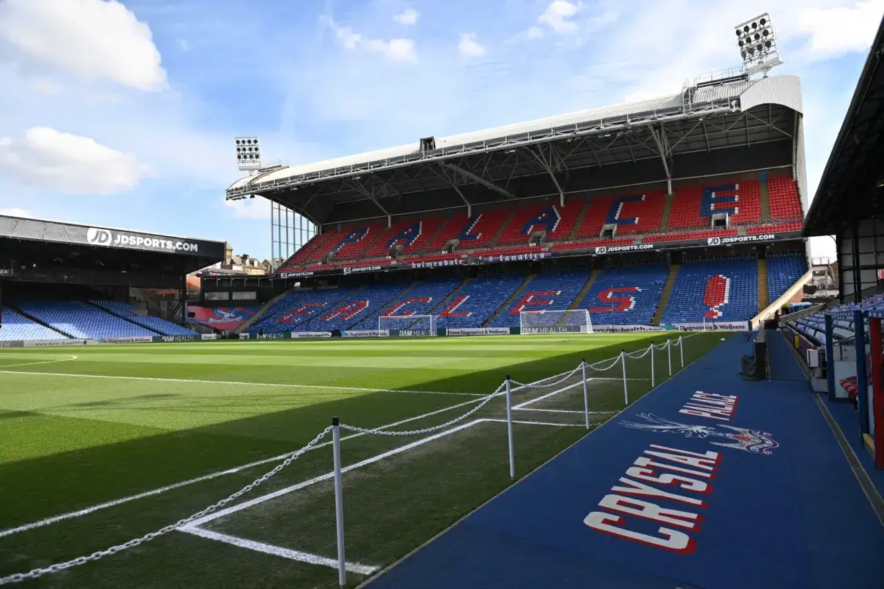 Puste trybuny stadionu Crystal Palace, z czerwonymi i niebieskimi siedzeniami tworzącymi napisy.