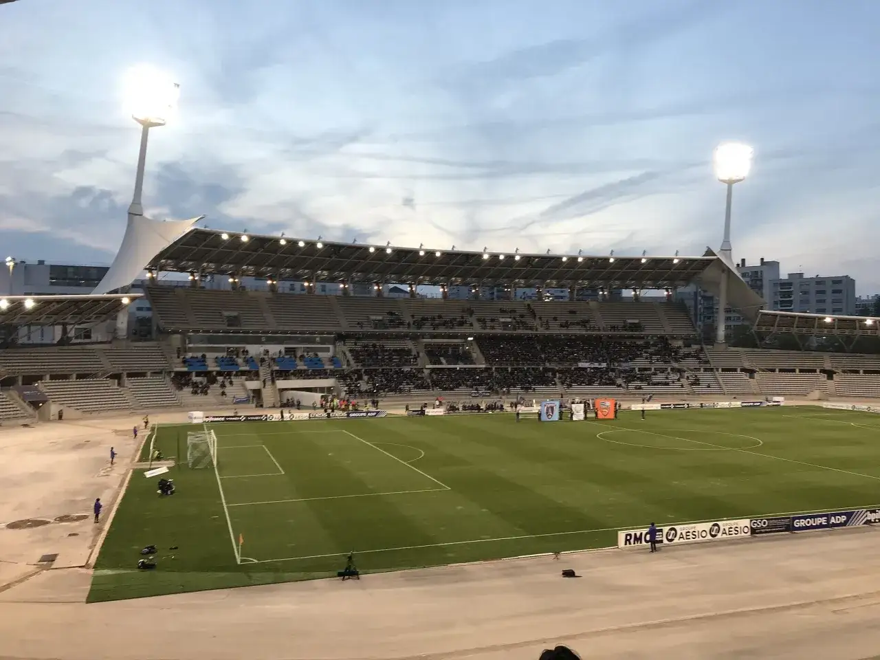 Stadion Sébastien Charléty w Paryżu, z oświetleniem i trybunami pełnymi widzów, gotowy na wieczorny mecz.