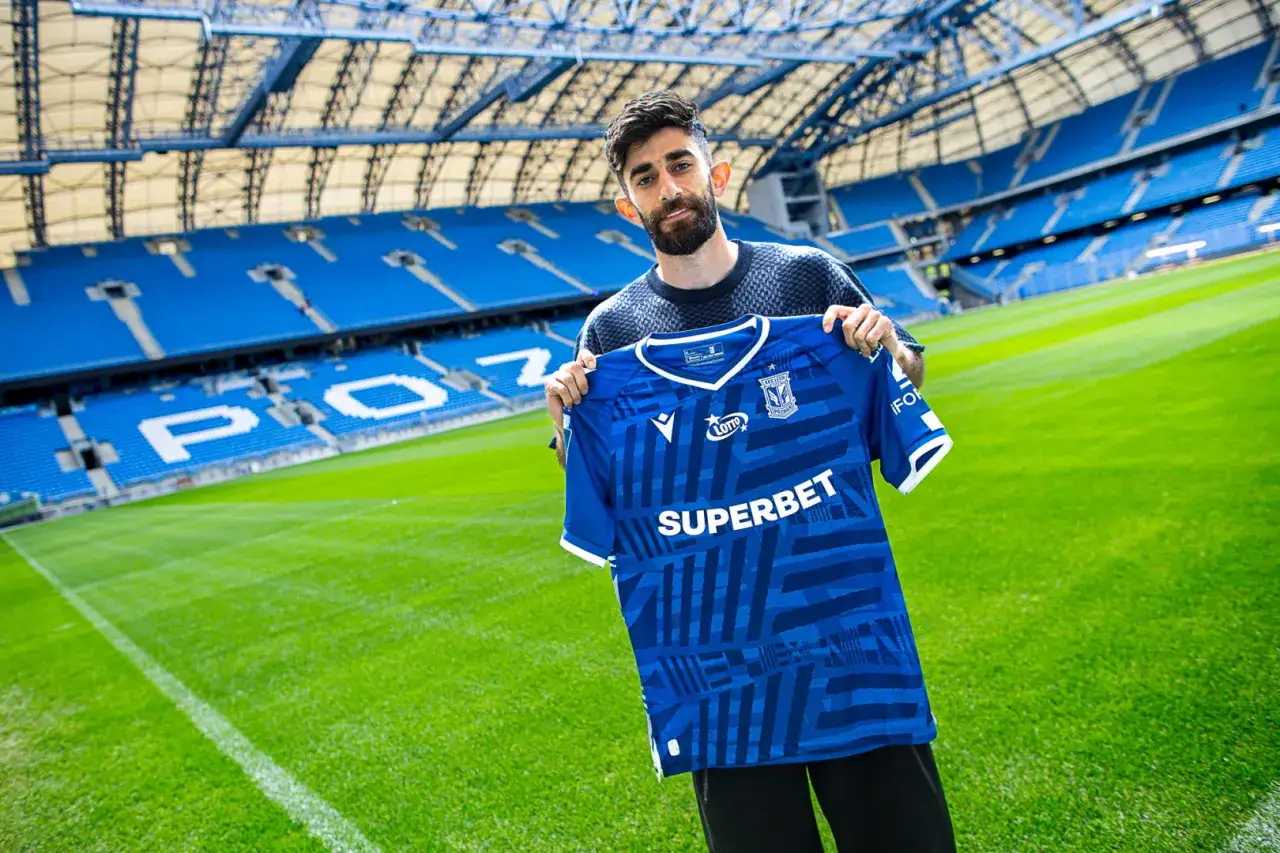 Ali Gholizadeh prezentuje nową koszulkę Lecha Poznań na tle stadionu.